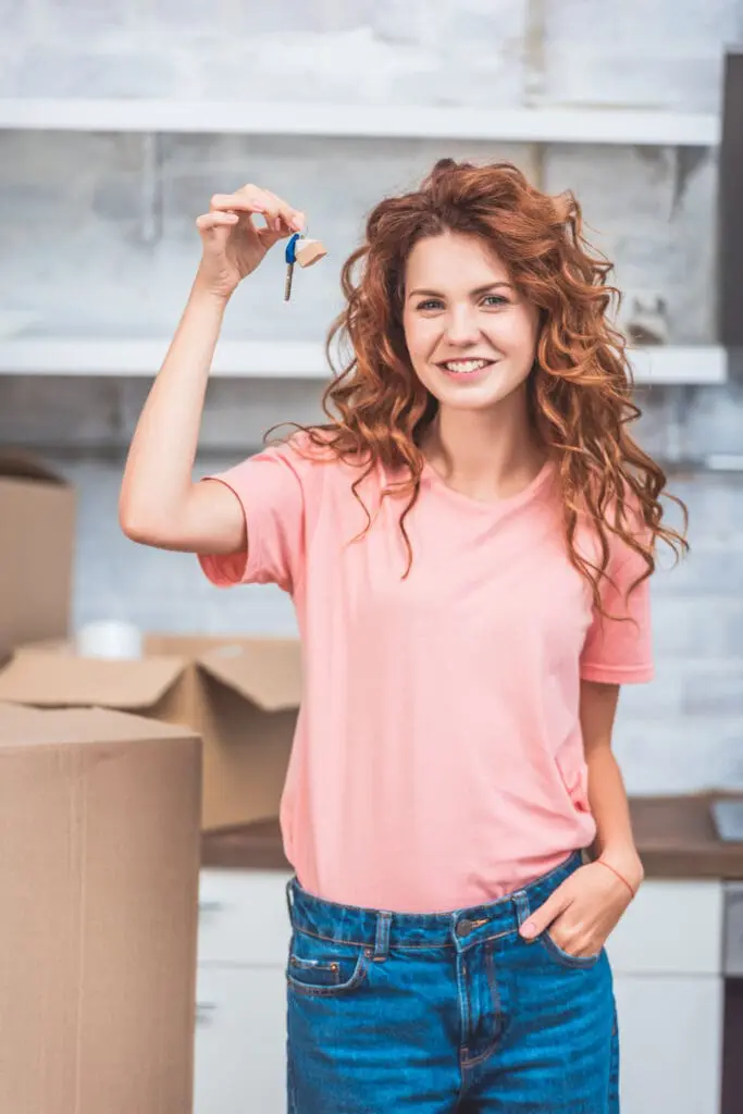 beautiful happy young woman holding key from new apartment and smiling at camera